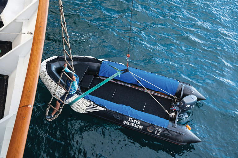 Crew member climbing down the ladder to enter the zodiac on Silver Galapagos. Silversea Cruises