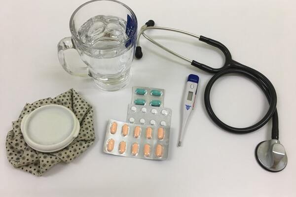 Glass of water with medicines, thermometer, stethoscope and ice bag. 600x400
