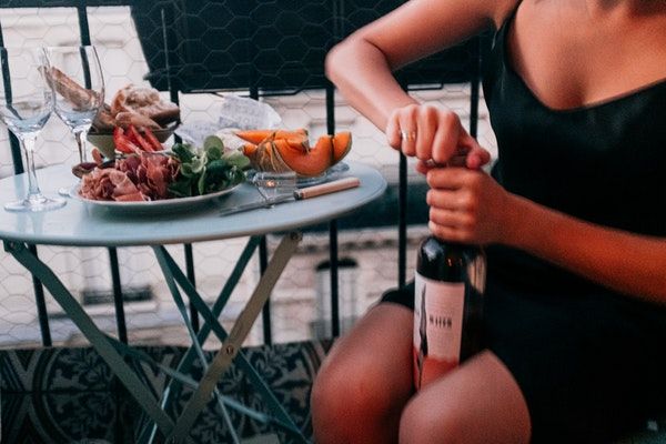 Lady opening a bottle of wine in front of a dry cured meat meal | px by Daria Shevtsova 600x400