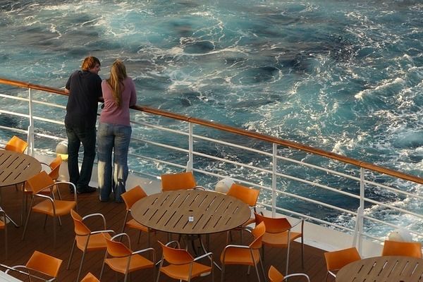 Two people standing at the back of a Carnival Cruise vessel enjoying the view looking forward for their coming vacation just after coming back from a shore excursion and ready to sail away   | 600x400