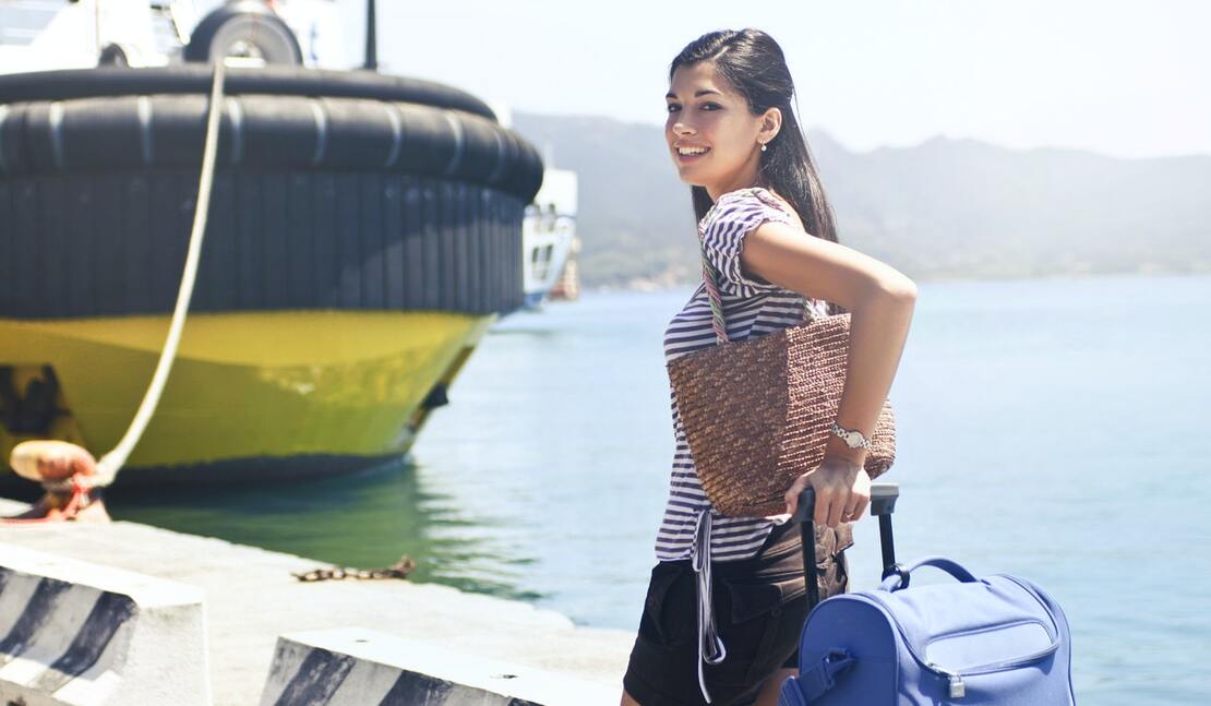 Woman standing on pier next to tug boat with her carry on bar and ready to start the cruise embarkation day process to finally board the ship | by Andrea Piacquadio