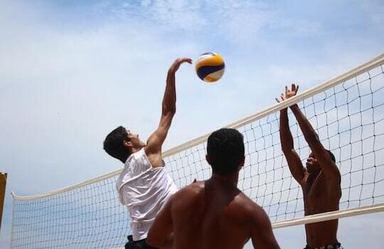 Photo of a group of young people playing beach volleyball in the sunset