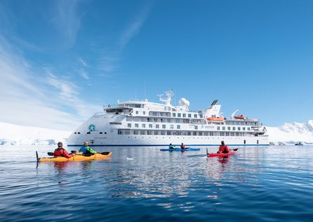 Greg Mortimer with a couple of passenger paddling around it  in Port Lockroy Antarctica | A.Bakker 446x317